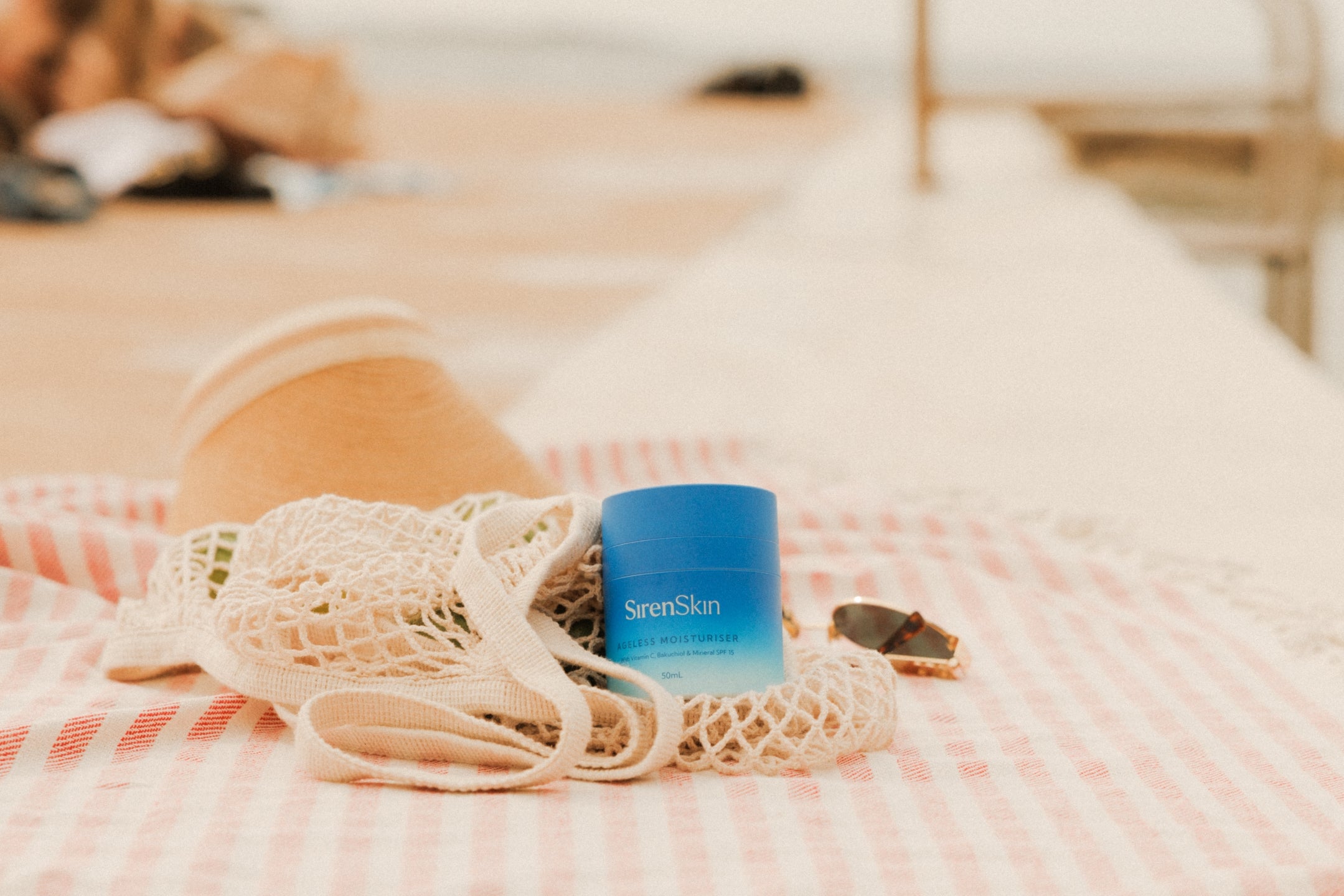 Container of skincare with reef-safe sunscreen and net bag on a beach towel.