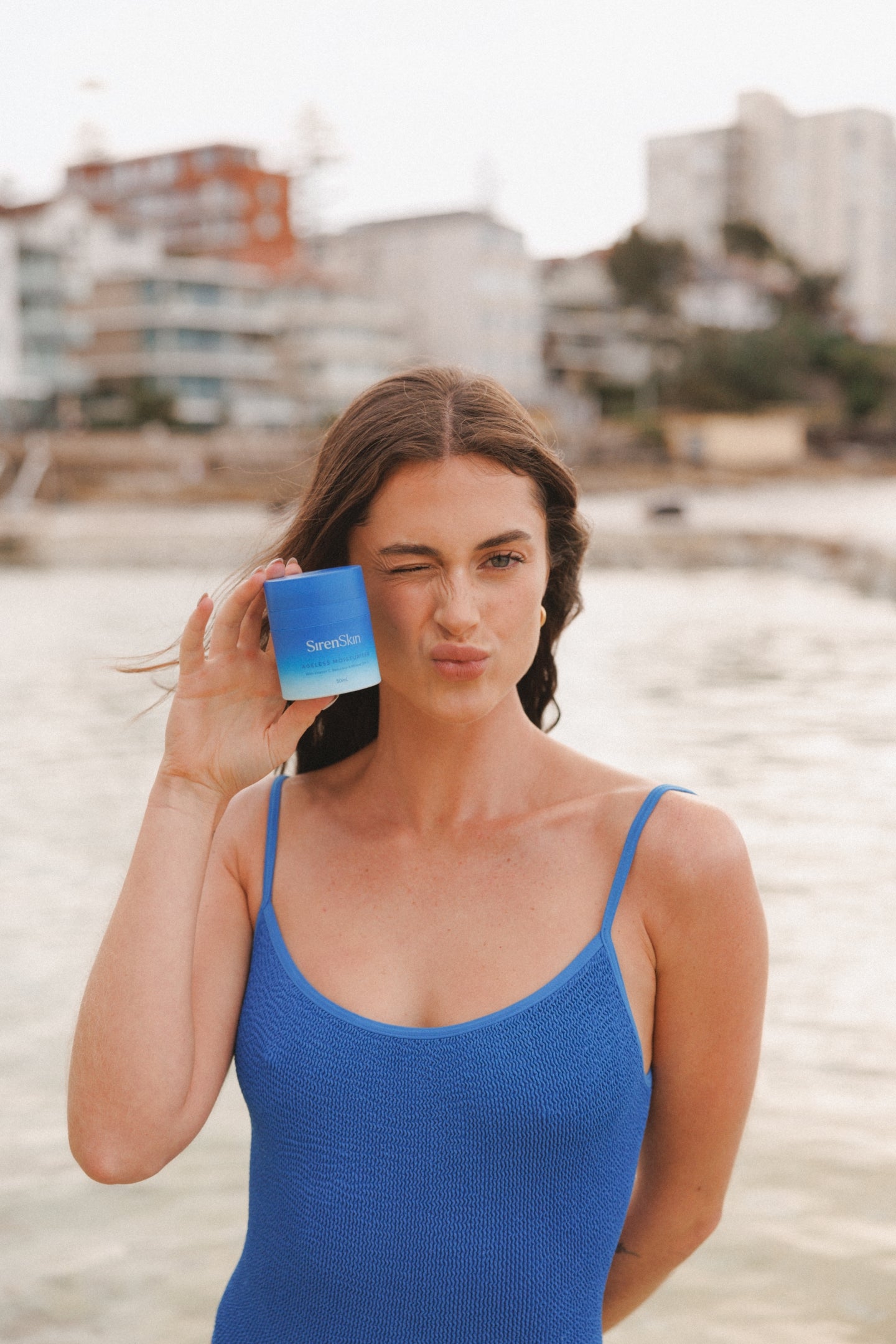 Woman holding blue siren skincare bottle on a beach